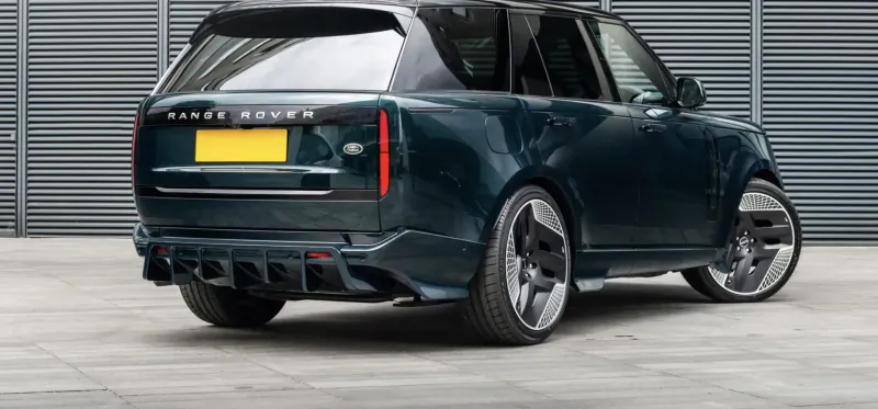 Rear view of Racing Green Range Rover with yellow license plate, quad exhausts, and large alloy wheels parked by gray shutters.