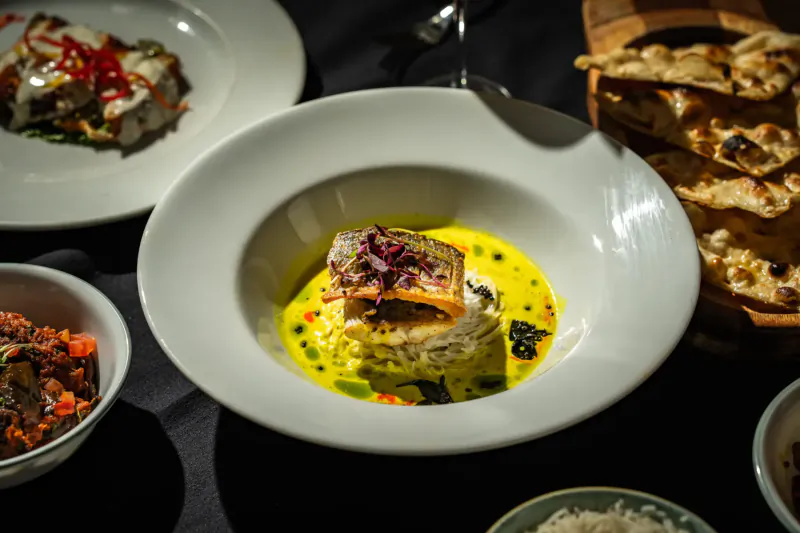 Indian dish of seared fish with edible flowers in yellow curry, served with naan, rice, and chutneys at Mint Leaf London.