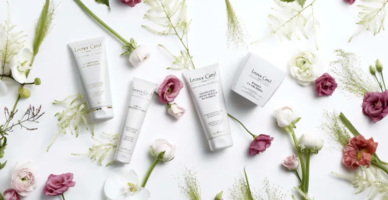 Leonor Greyl hair care products on white background with pink and white flowers and green leaves.