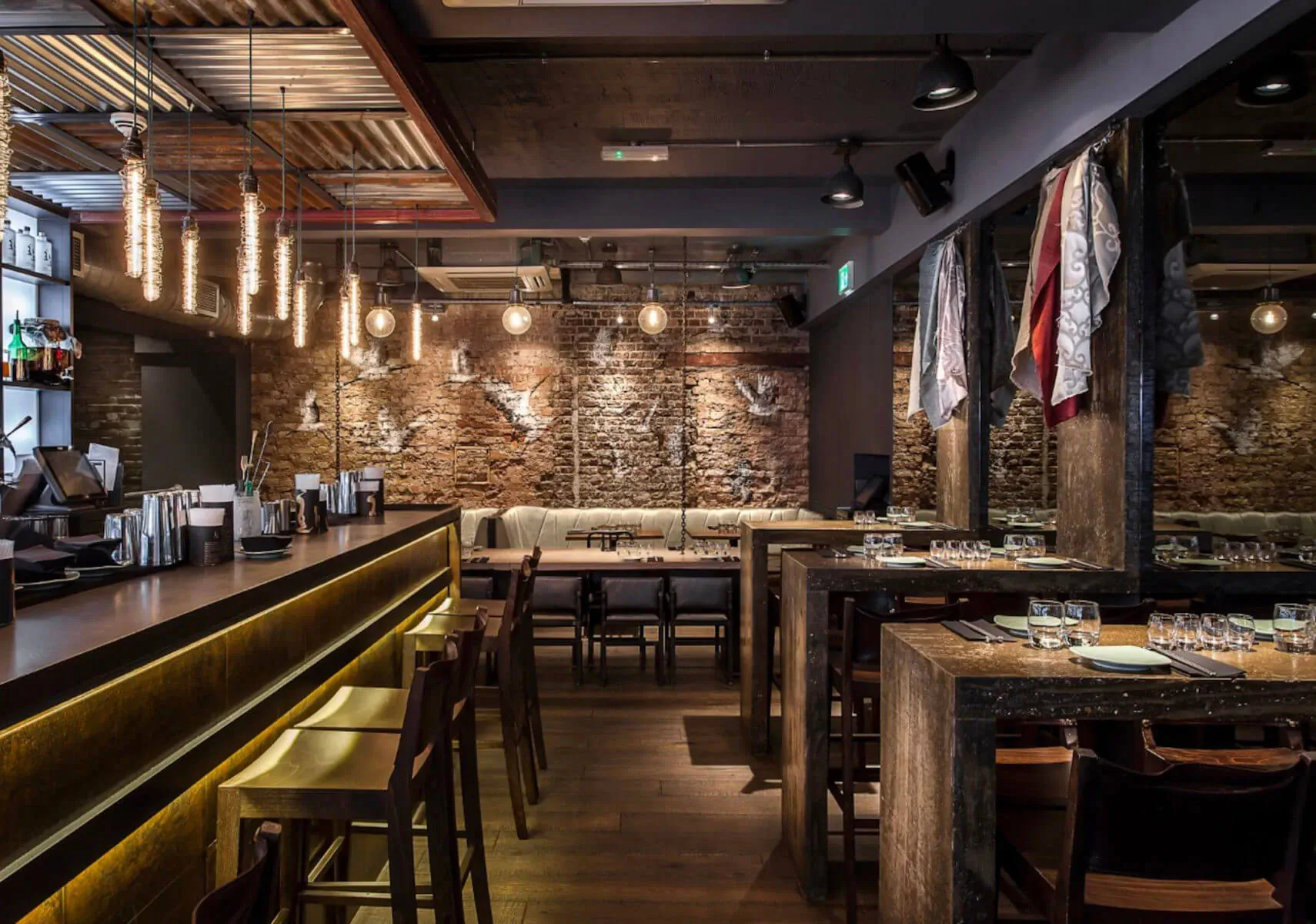 Modern industrial bar in Carnaby London with brick walls, pendant lights, wooden bar, stools, and tables.