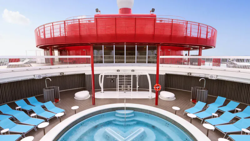 Red Virgin Cruises ship deck with central blue hot tub, blue loungers, showers, and railings under blue sky