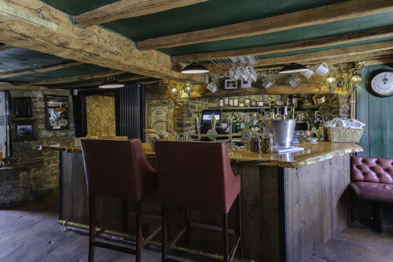 Rustic wooden bar at Nut Tree Inn with green ceiling, red stools, pendant lights, champagne bucket, and stone walls.