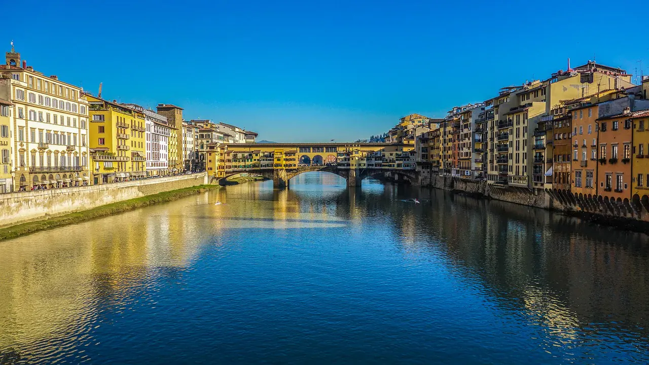 Ponte Vecchio bridge spanning the Arno River in Florence, lined with colorful historic buildings under blue sky.