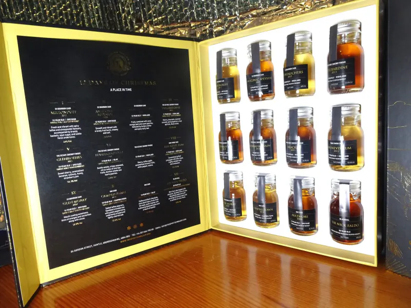 Open gold luxury whisky gift box with 12 assorted amber-filled bottles and French labels like 'Les Whiskies'.