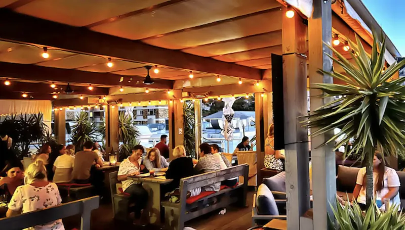 Outdoor restaurant on Kloof Street, Cape Town, with patrons dining under warm string lights and plants at dusk.