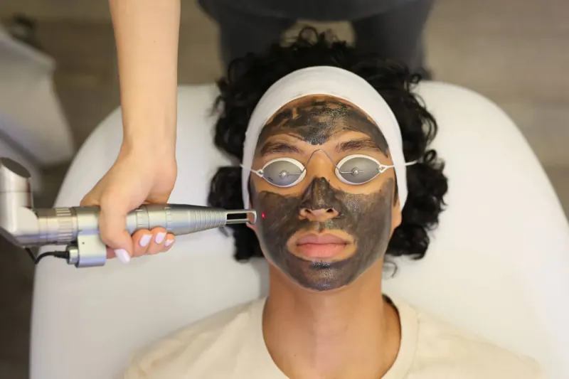 Close-up of person with black facial mask and protective goggles during laser treatment by beautician