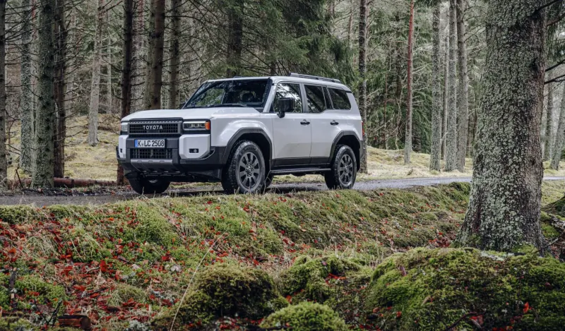 White Toyota Land Cruiser on forested road with autumn mossy embankment