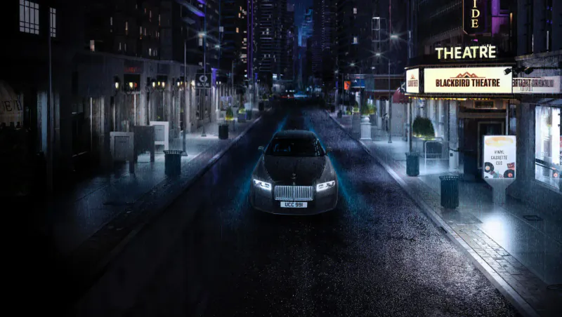 Black Badge Rolls-Royce Ghost with glowing blue headlights driving wet neon-lit city street at night toward marquee theatre.