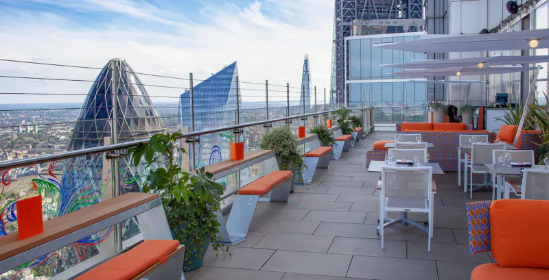 SushiSamba rooftop terrace with orange seating, tables, plants, and panoramic London skyline view including Shard and Gherkin.