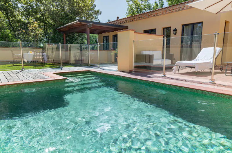 Inviting turquoise pool at Terre Blanche oasis in Provence, with lounge chairs, pergola, and ochre house amid trees.
