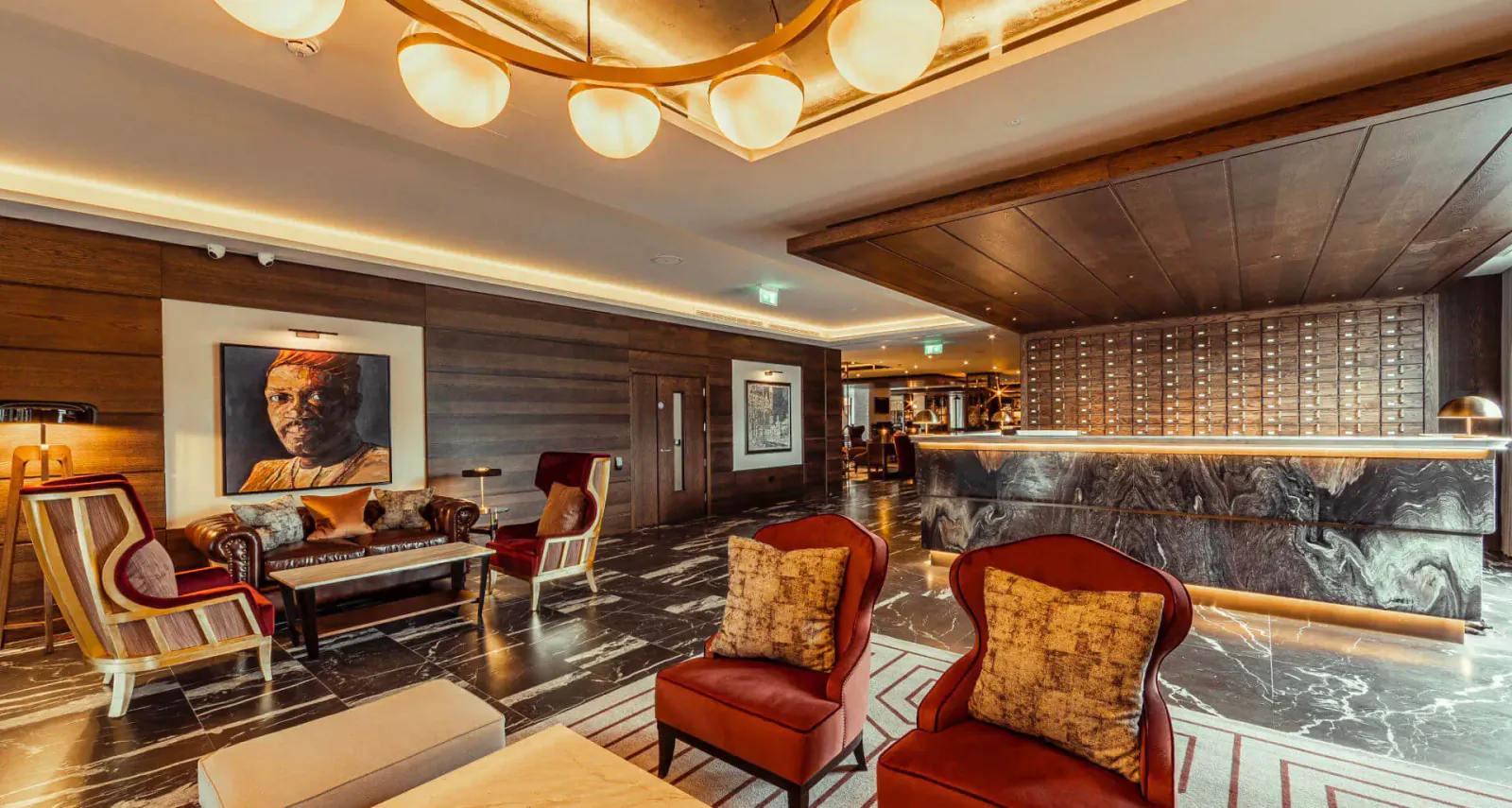 Luxury lobby at The Fellows House Cambridge with large portrait, red armchairs, marble reception desk, and warm lighting