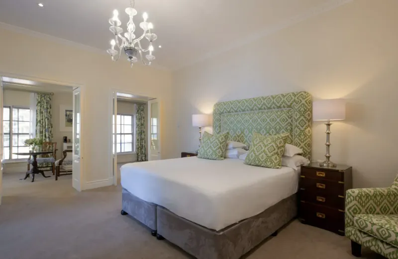 Elegant hotel bedroom with green upholstered headboard, king bed, chandelier, and armchair in The Marine Hotel Hermanus