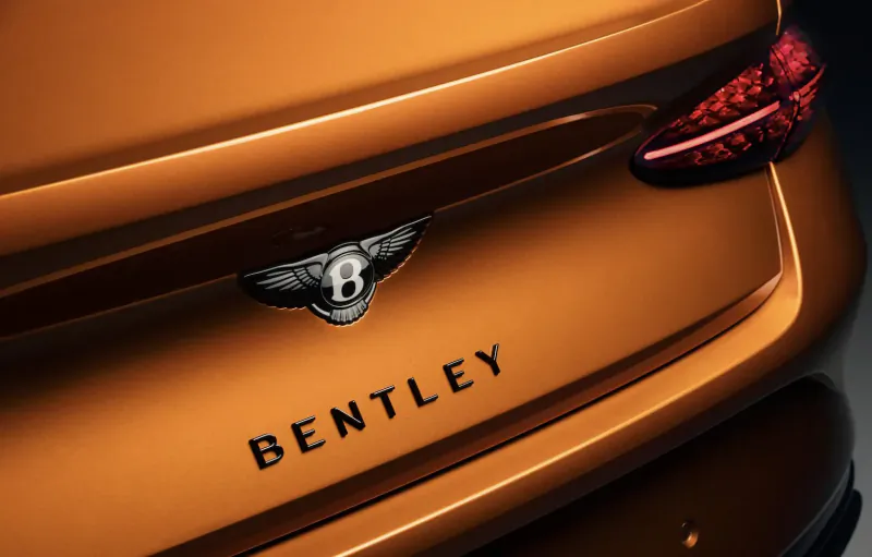 Rear view of orange Bentley Continental GT Black Edition with glowing taillights, Bentley wings badge, and 'BENTLEY' text.