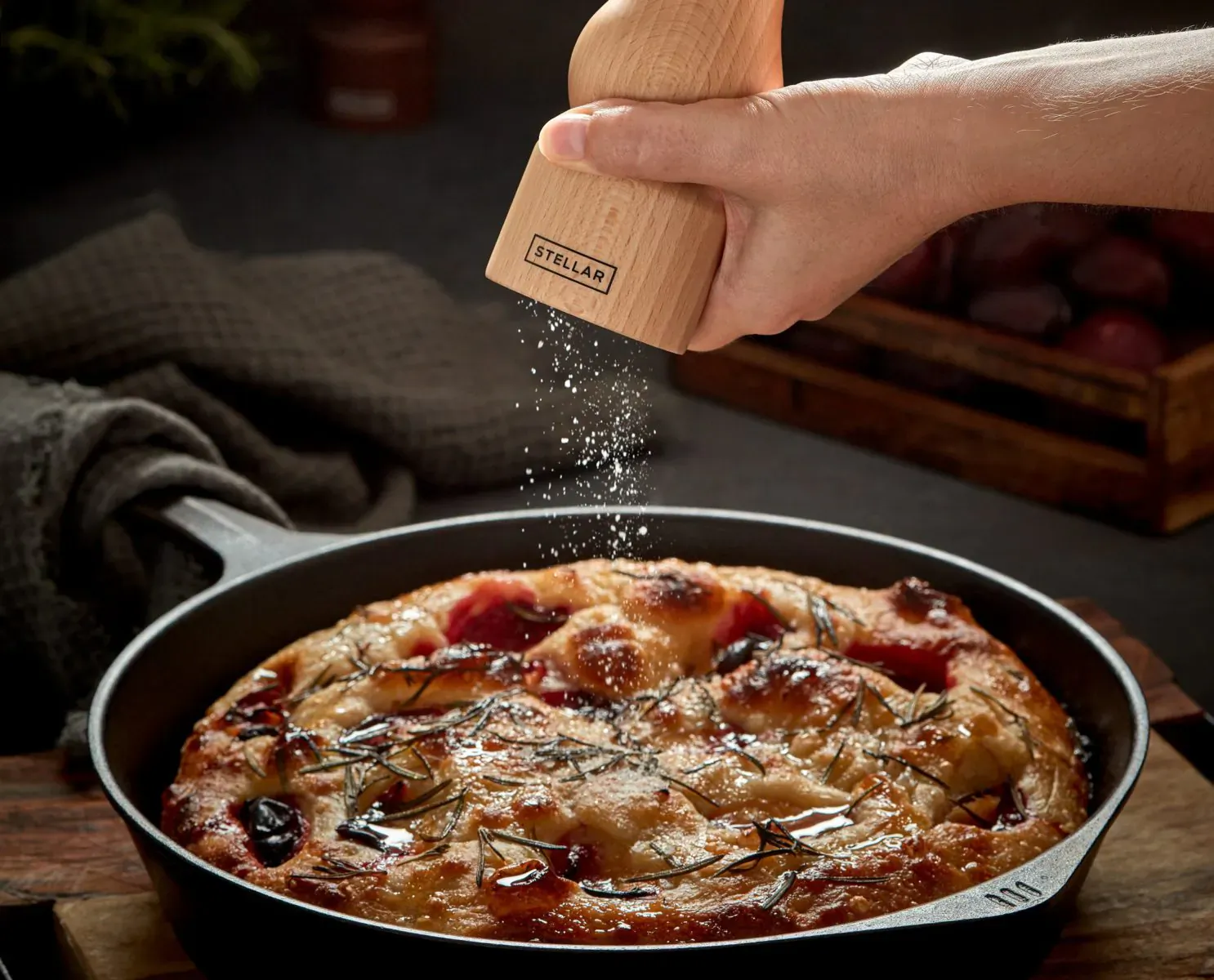 Hand grinds salt from 'Stellar' wooden mill over rosemary focaccia in cast iron pan on wooden board