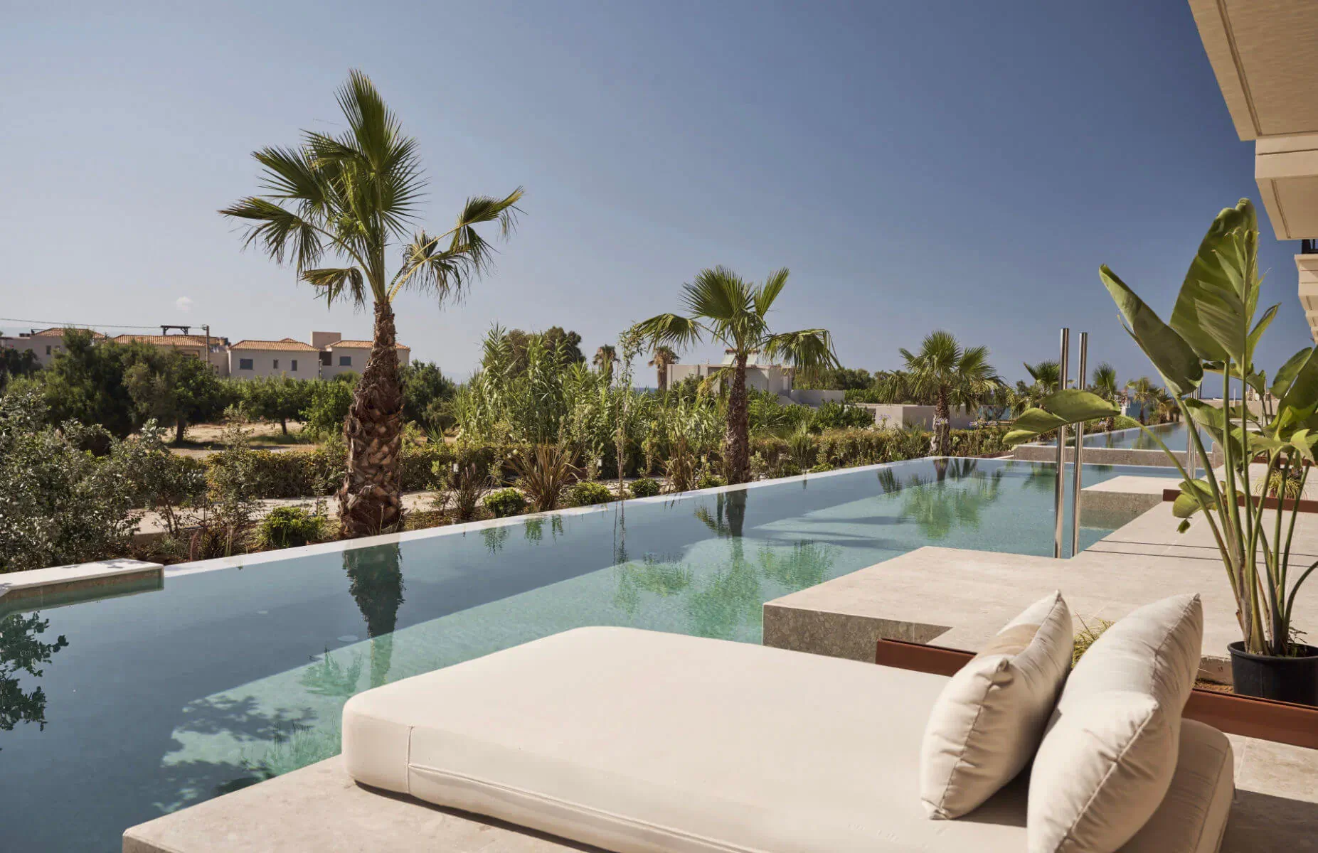 Infinity pool at Asterion Suites & Spa, Crete, with lounge bed, palms, and sea views under blue sky.