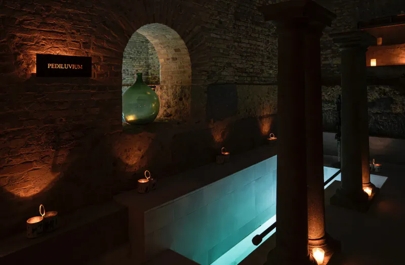 Candle-lit Aire Ancient Baths in London: arched brick walls, stone columns, green vase, glowing turquoise pool.