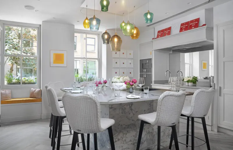 Bright kitchen for cooking masterclass at Pied à Terre with colorful pendant lights, marble island set for dining, flowers, and window views.