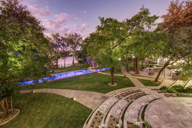 Aerial view of Palm River Hotel grounds at dusk: blue pool, lush trees, lawns, paths, and Zambezi River near Victoria Falls.