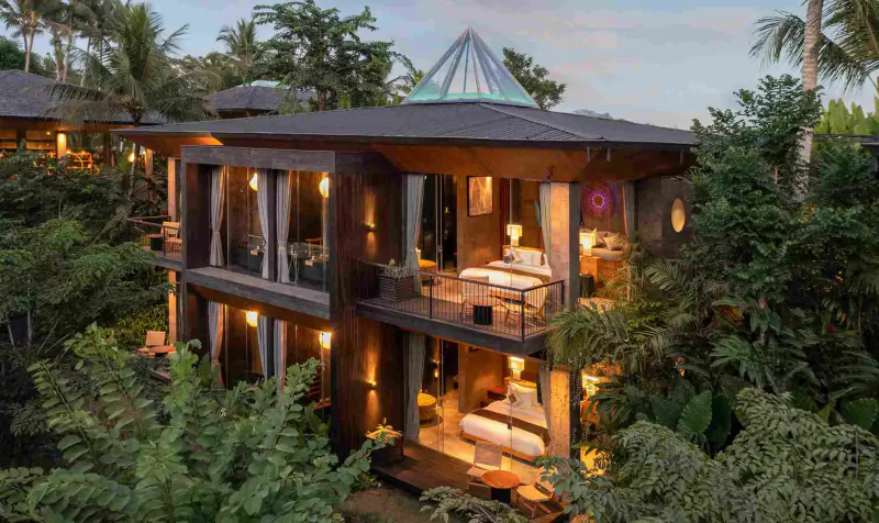 Luxurious two-story GDAS Bali retreat villa with pyramid roof, balcony, lit warmly amid lush tropical greenery at dusk