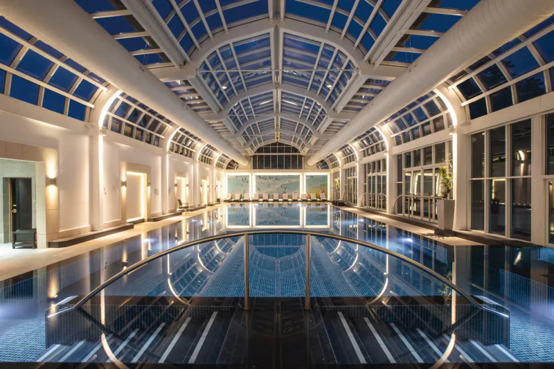 Elegant indoor pool at Four Seasons Hampshire with arched glass ceiling and evening light reflections.