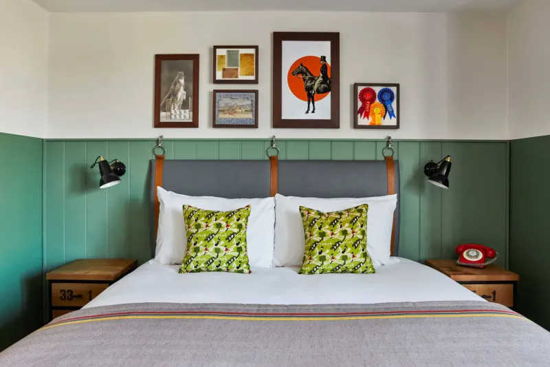 Cozy Hotel Indigo Chester bedroom with green pillows, gray upholstered bed, art wall, retro phone on nightstand.