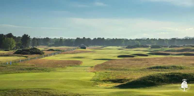 Carnoustie Links golf course with rolling green fairways, sandy bunkers, and distant trees under partly cloudy sky
