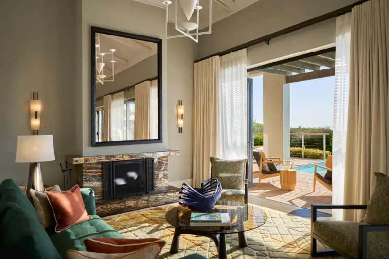 Luxurious living room at Delaire Graff Estate with fireplace, plush seating, pool view through open doors to Cape Winelands.
