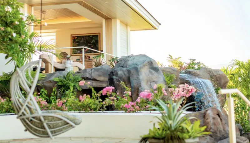 Luxury villa patio with hanging swing, rock waterfall, pink flowers, tropical plants, and ocean view.