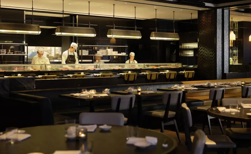 Nobu Hotel Marylebone: Chefs in white hats preparing sushi at sleek black sushi bar with tables and pendant lights.