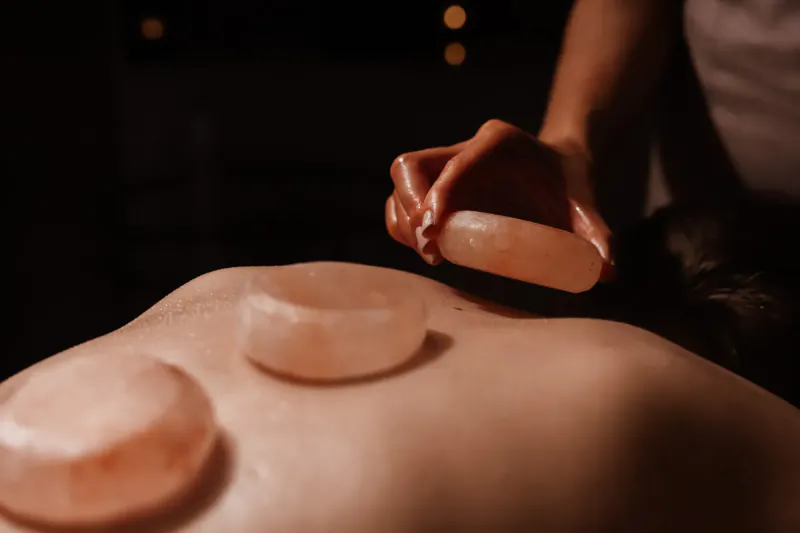 Therapist placing pink Himalayan salt stones on client's bare back during spa treatment