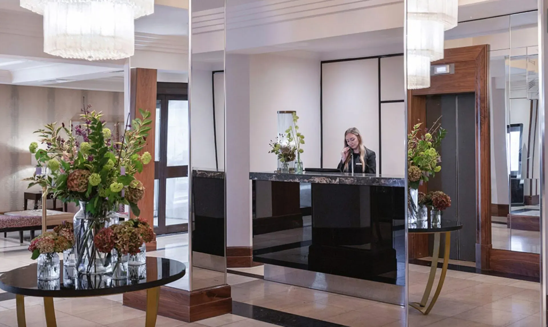 Elegant hotel lobby at The Bristol with black reception desk, staff on phone, floral arrangements, chandeliers, and mirrors.