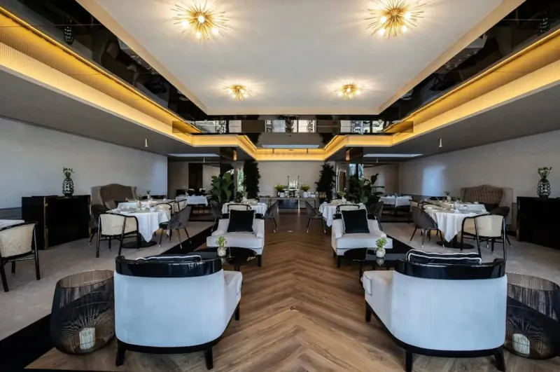 Elegant dining room at VINHA Boutique Hotel with white tables, black chairs, plants, and glowing ceiling lights.