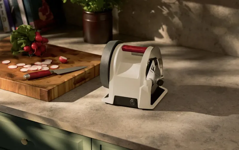 White vegetable slicer with red handle on kitchen counter beside chopped red radishes and cutting board