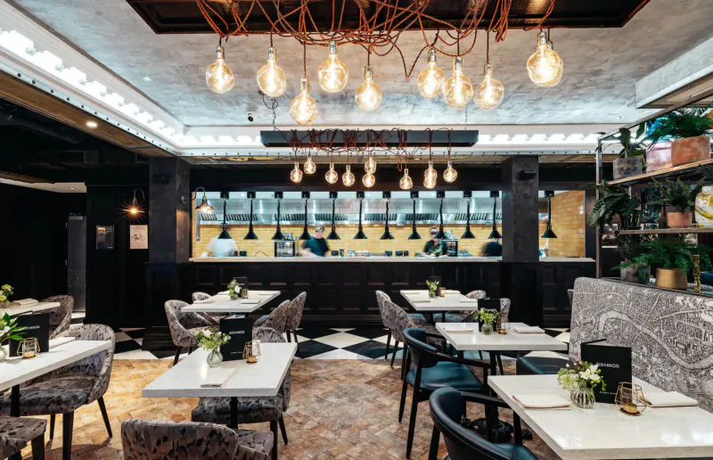 Elegant Six by Nico restaurant interior in Canary Wharf with pendant lights, marble tables, plants, and bar.