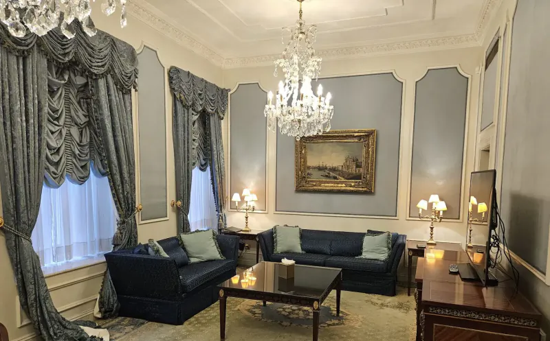 Elegant lounge in Bentley Hotel, Kensington: navy leather sofas, crystal chandelier, classic painting, tall windows with drapes.