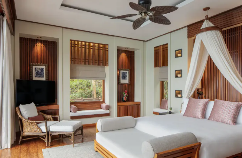 Luxurious Anantara Maia Seychelles villa bedroom with wooden walls, canopy bed, ceiling fan, and garden view.