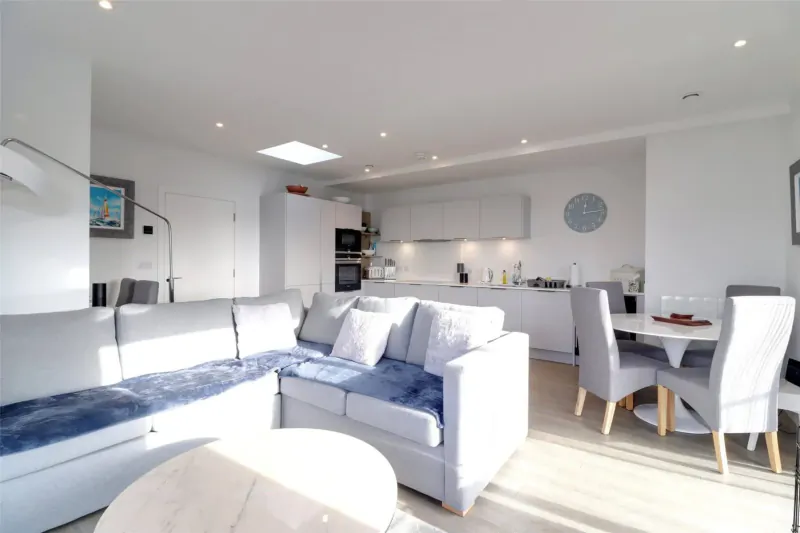 Bright modern open-plan living room and kitchen in Woolacombe Bay stay, with L-shaped sofa, round table, and skylight.