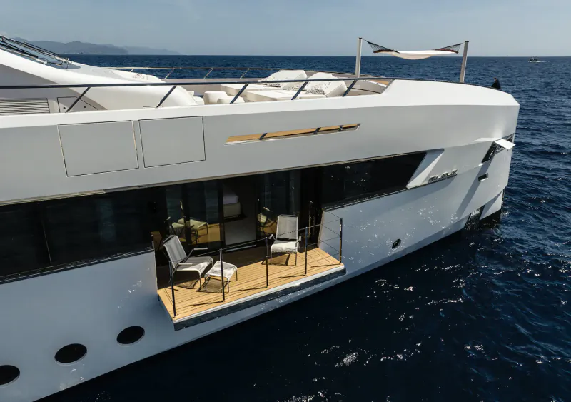 White luxury yacht Milele with wooden deck balcony, chairs, and ocean view at sea.