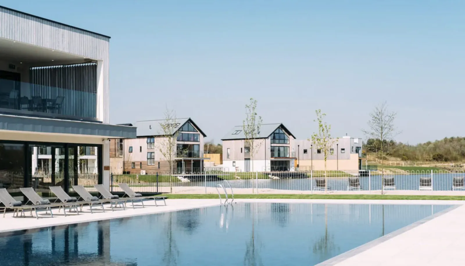 Modern Luxuria buildings and lounge chairs beside a large infinity pool at Silverlake Dorset, with lake view.