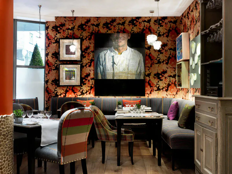 Chic Soho Hotel restaurant interior with large portrait of chef in uniform, ornate orange floral walls, cozy booth seating, and dining table.