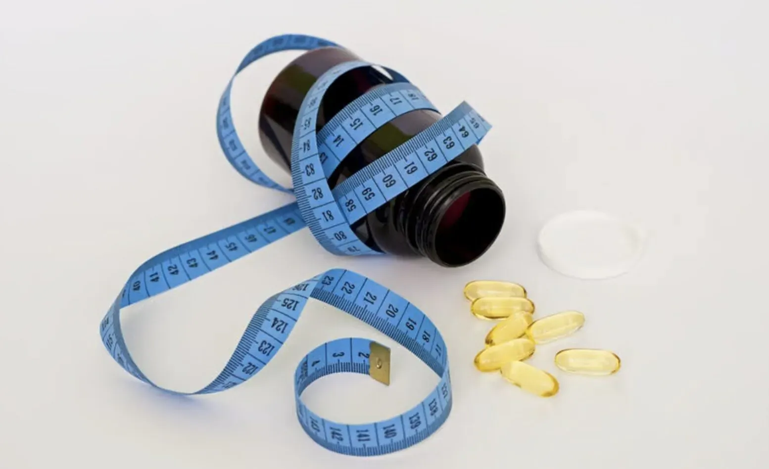 Brown prescription bottle wrapped in blue measuring tape, with scattered yellow weight loss pills beside it