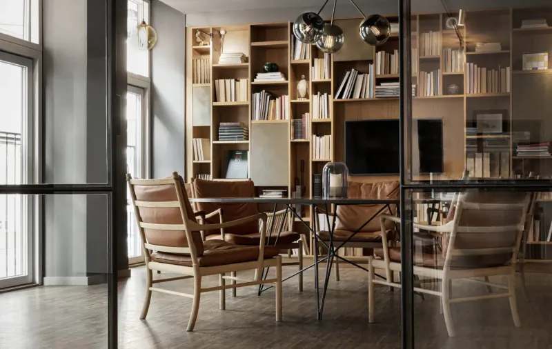 Modern Hotel SP34 gallery in Copenhagen with wooden bookshelves, leather chairs around glass table, pendant lights, city view.