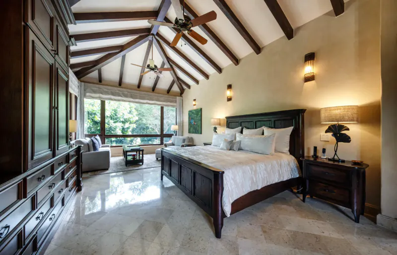 Luxurious bedroom in private villa with wooden king bed, ceiling fan, large window to greenery, warm lighting