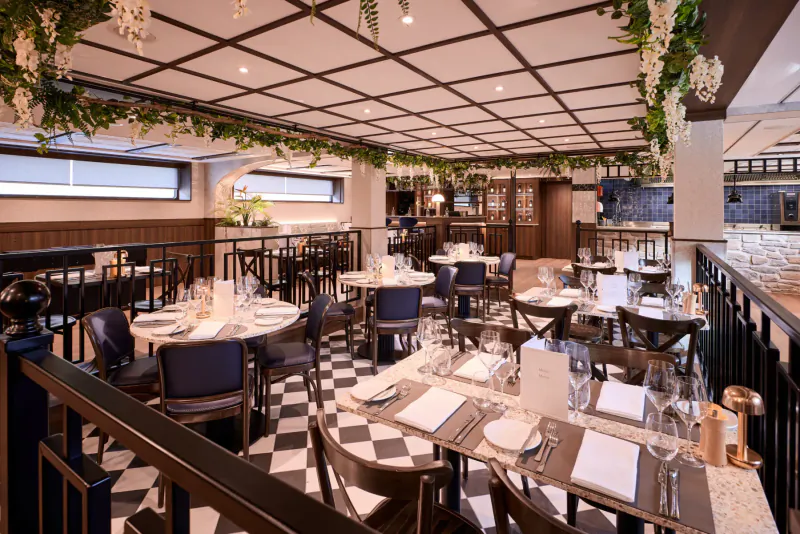 Elegant cruise ship dining room with checkered floors, wisteria garlands, and neatly set tables for gourmet voyage.