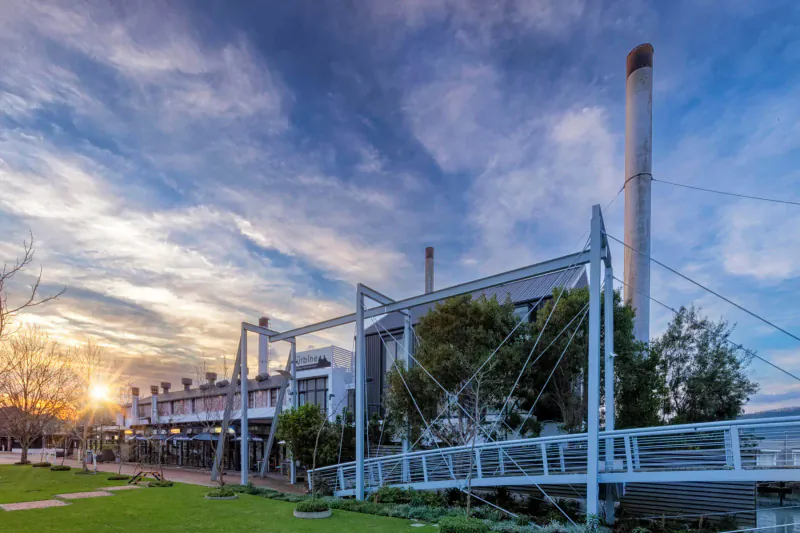 Turbine Hotel luxury boutique exterior with smokestacks, metal walkways, trees, lawn, and sunset sky.