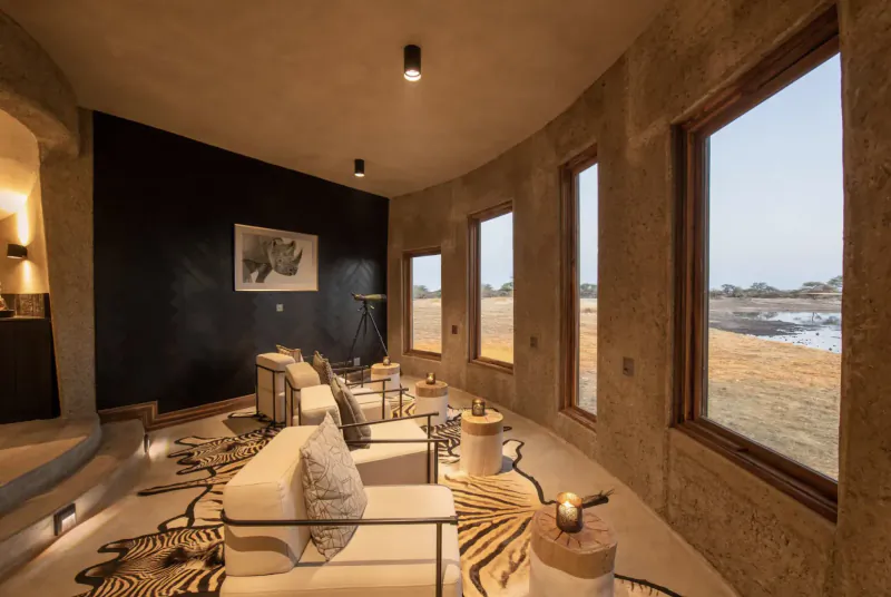 Luxurious curved lounge at Camp Kala with white sofas, zebra rug, rhino art, and Etosha savanna view