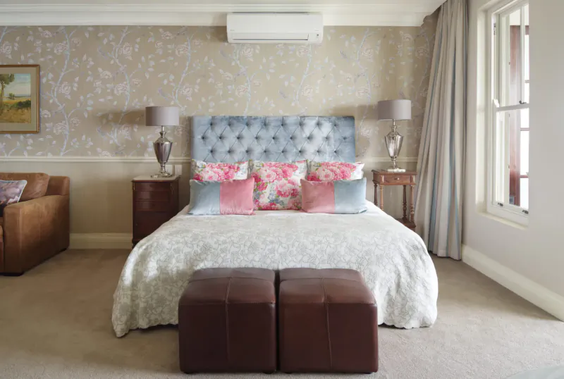 Elegant bedroom at 21 Nettleton Boutique Hotel with tufted blue headboard, pink pillows, white bedspread, lamps, and window.