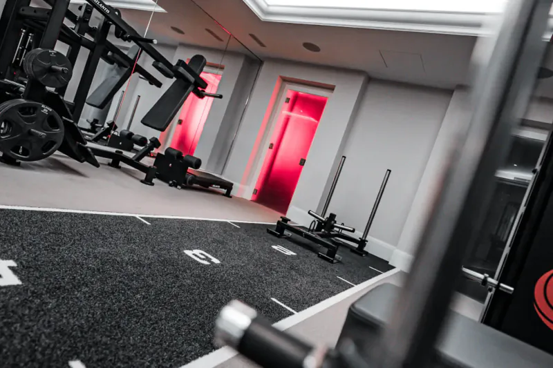 Modern gym interior with black weight racks, red door, and rubber floored training area at The Body Lab.