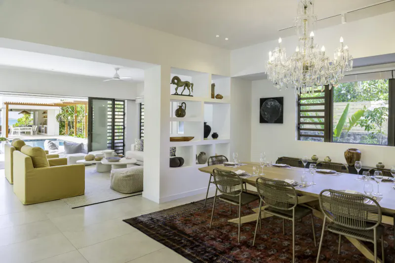 Spacious open-plan living and dining area in Villa Diamond, Mauritius, with yellow sofas, wooden table, chandelier, and tropical views.