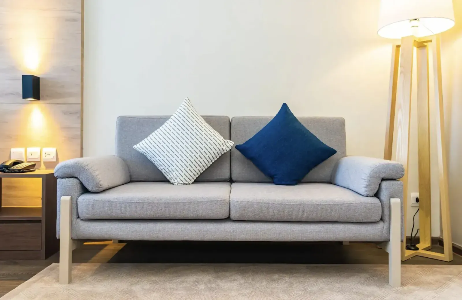 Modern gray loveseat with white and navy pillows in cozy living room with warm lamps and wood wall.